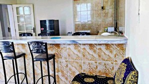 A kitchen with a marble countertop, two bar stools, a refrigerator, and a window with a view. - Superb F2 Apartment With INCREDIBLE Panoramic View (Souk El Ténine)