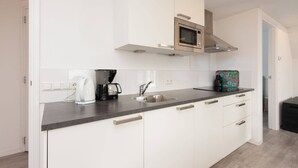 Une cuisine moderne avec des armoires blanches, un évier en acier inoxydable, un four à micro-ondes et une machine à café.
