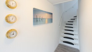 Un escalier aux marches blanches et aux rampes noires, menant à un palier où est accrochée une peinture représentant un coucher de soleil sur l’eau.