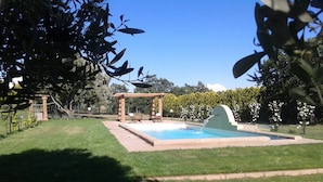 Een achtertuin met een zwembad, een pergola en een verzorgd gazon.