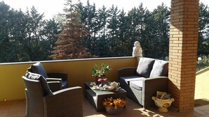 Een balkon met rieten meubels, een beeld en een potplant.