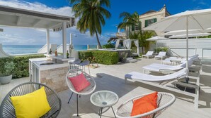 Un espace de détente extérieur baigné de soleil, avec des fauteuils blancs, un petit bar et une vue sur l’océan.
