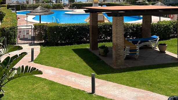 A resort pool area with a clear view of the ocean, surrounded by palm trees and a building with multiple balconies. - La Duquesa Port, South facing ground floor apartment, with large terrace (Puerto Duquesa)
