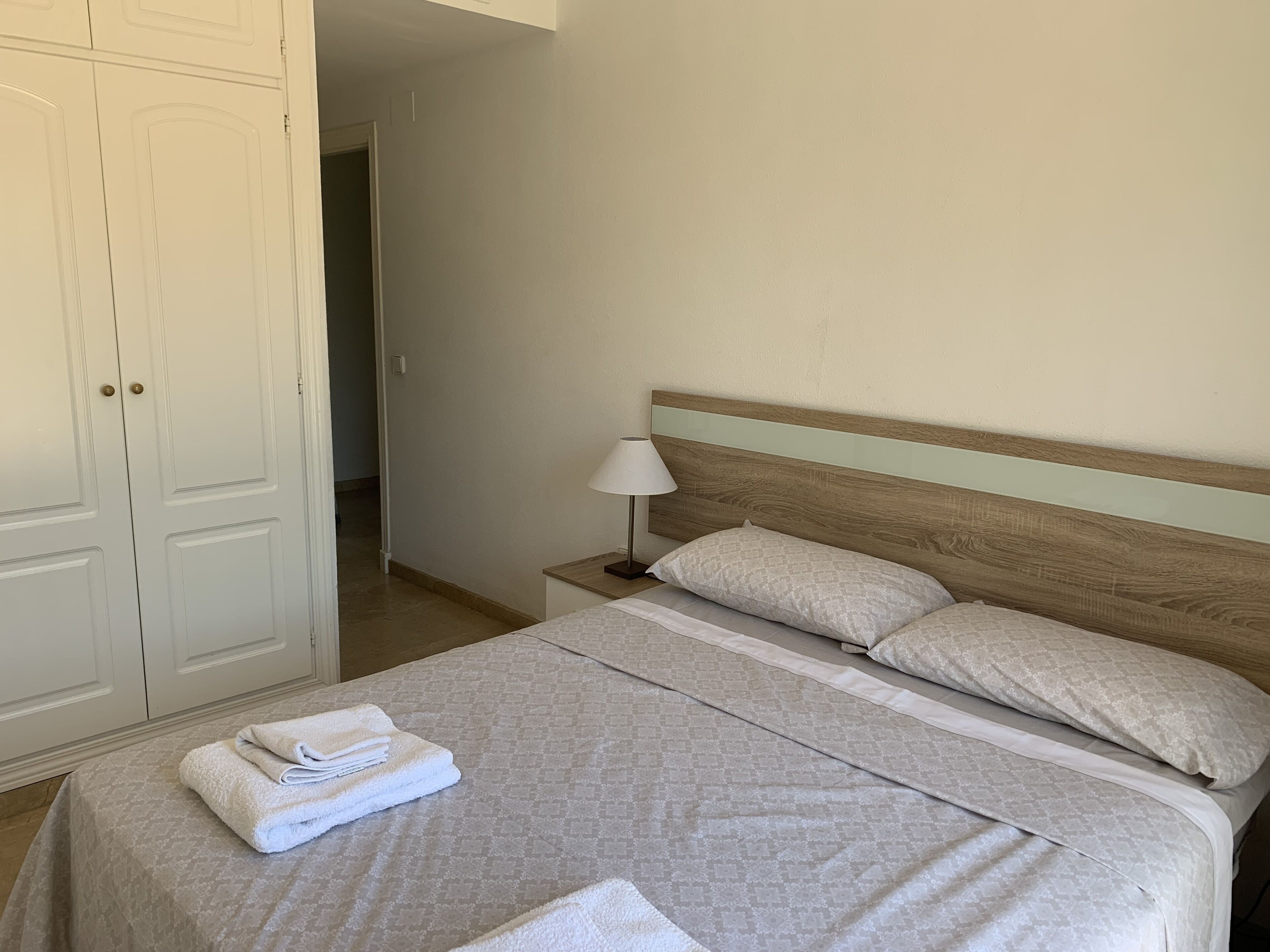Een net opgemaakt bed met een beddekleed met patroon, twee kussens en opgevouwen handdoeken opzij.
