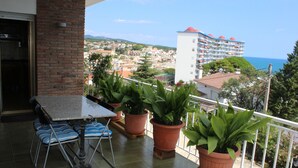 Ein Balkon mit Tisch und Stühlen, Blumentöpfen und Blick auf eine Küstenstadt sowie ein Hotel.