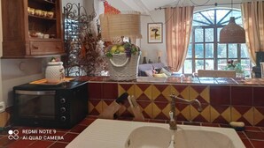 A kitchen with a wooden cabinet, a microwave, a sink with a vintage faucet, and a window with curtains. - Shed renovated with charm, swimming pool and bucolic garden at the foot of the Luberon (Cheval-Blanc)