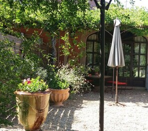 Un jardin agrémenté de grands pots de plantes et d’une pergola surmontée d’un parasol.