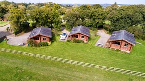 Drei Holzblockhäuser mit Solaranlagen, umgeben von üppigem Grün und einem eingezäunten Feld.