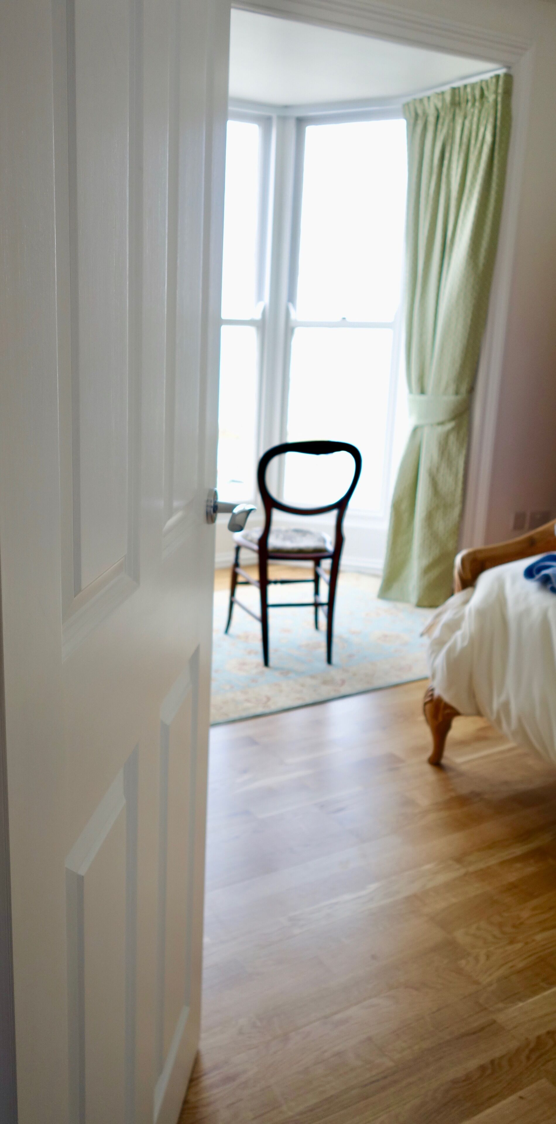 Ein Schlafzimmer mit Holzboden, einem Bett, einem Sessel und einem Fenster mit grünen Vorhängen.
