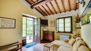 Una sala de estar acogedora con un sofá, una mesita, un banco y un aparador de madera. Hay un televisor sobre un mueble bajo, un mapa en la pared y una ventana con vistas a zonas verdes.