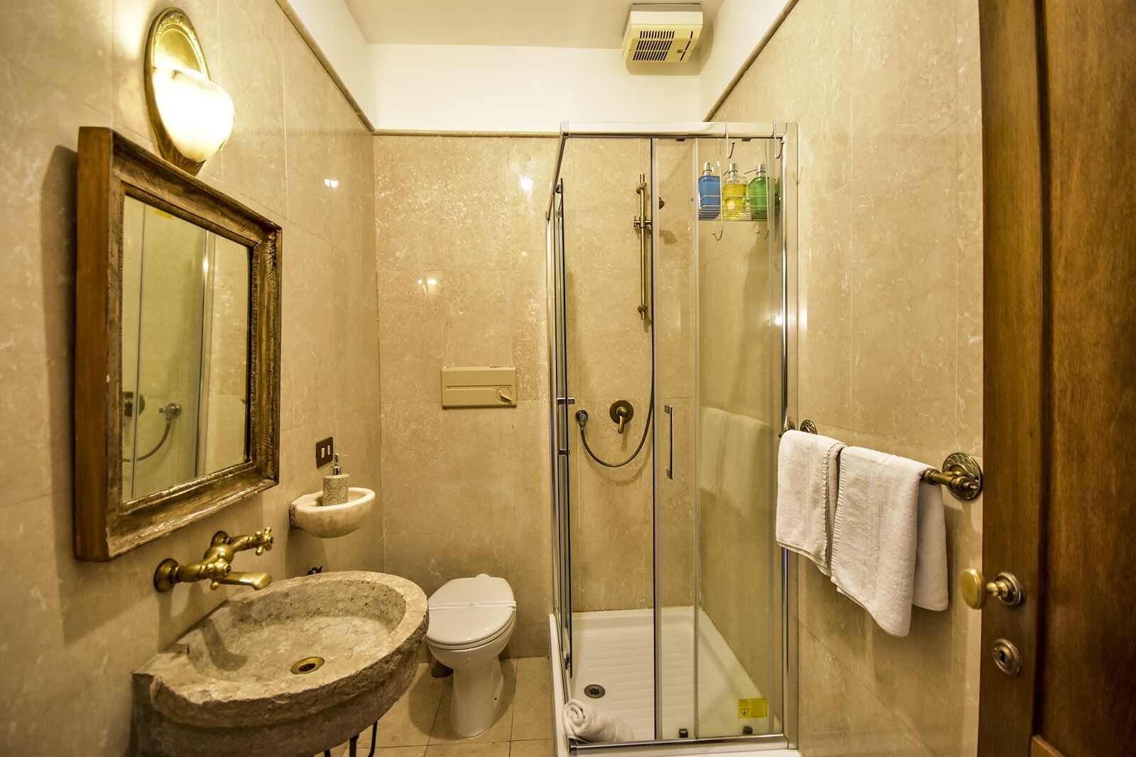 A bathroom with a marble sink, a toilet, a glass-enclosed shower, a towel rack, and a mirror with a light fixture.