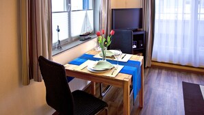 Uma área de jantar com uma mesa posta para dois, um vaso com flores e um modelo de veleiro no parapeito da janela.