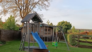 A wooden play structure with a slide and swings in a backyard. - Cozy vacation home for up to 8 pers., 4 bathrooms, W- Lan, sauna house, dog allowed  (Trendelburg)