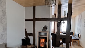 A cozy living room with a fireplace, a sofa, a dog bed, and a dining area with wooden chairs and a table. - Cozy vacation home for up to 8 pers., 4 bathrooms, W- Lan, sauna house, dog allowed  (Trendelburg)