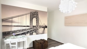 Ein Schlafzimmer mit einer großen Wandmalerei einer Brücke, einem weißen Schreibtisch mit einer Vase und einer Holzkiste.