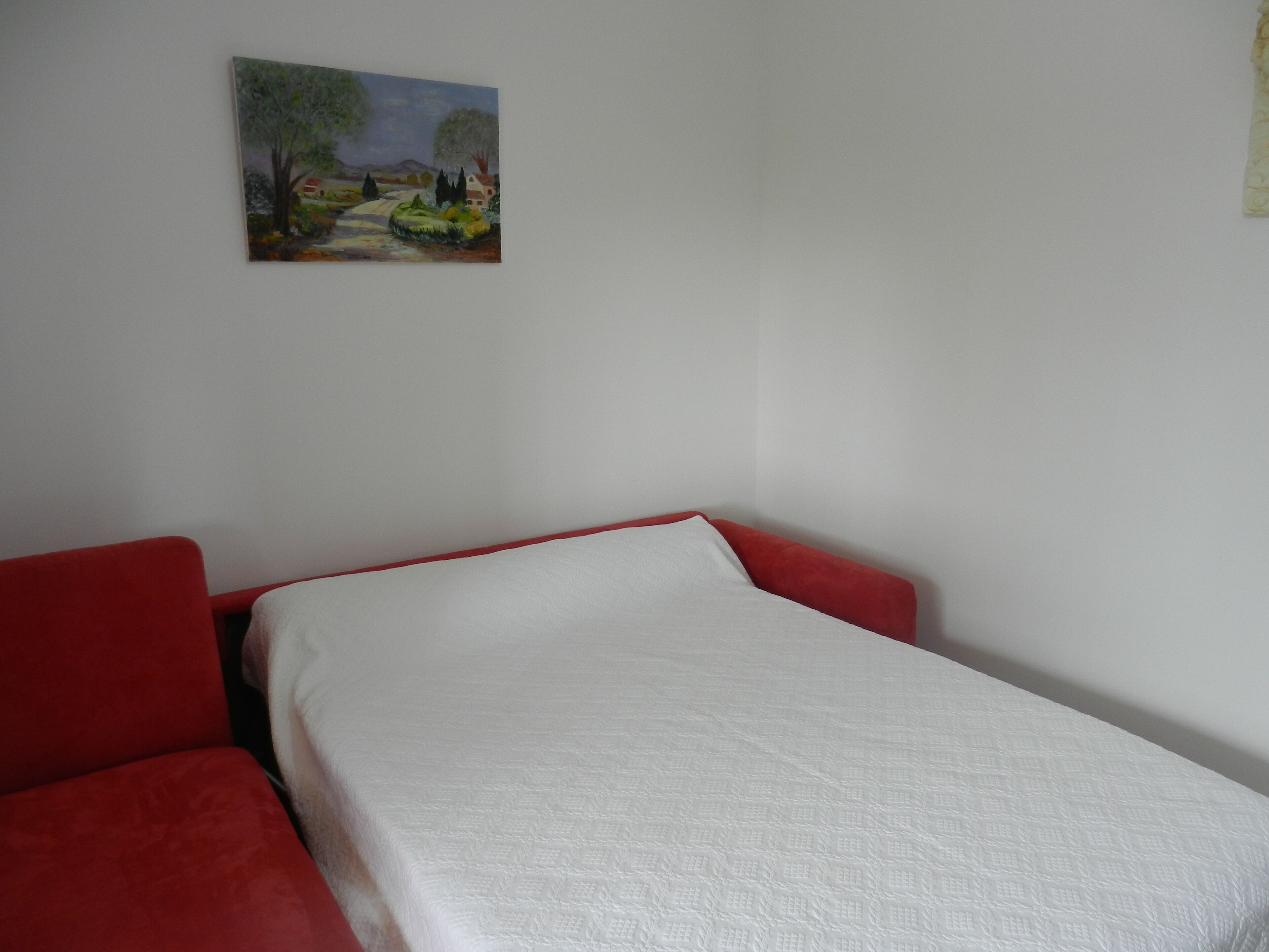 Ein Zimmer mit einem Einzelbett, einem roten Kopfteil, weißer Bettwäsche und einem Landschaftsbild an der Wand.