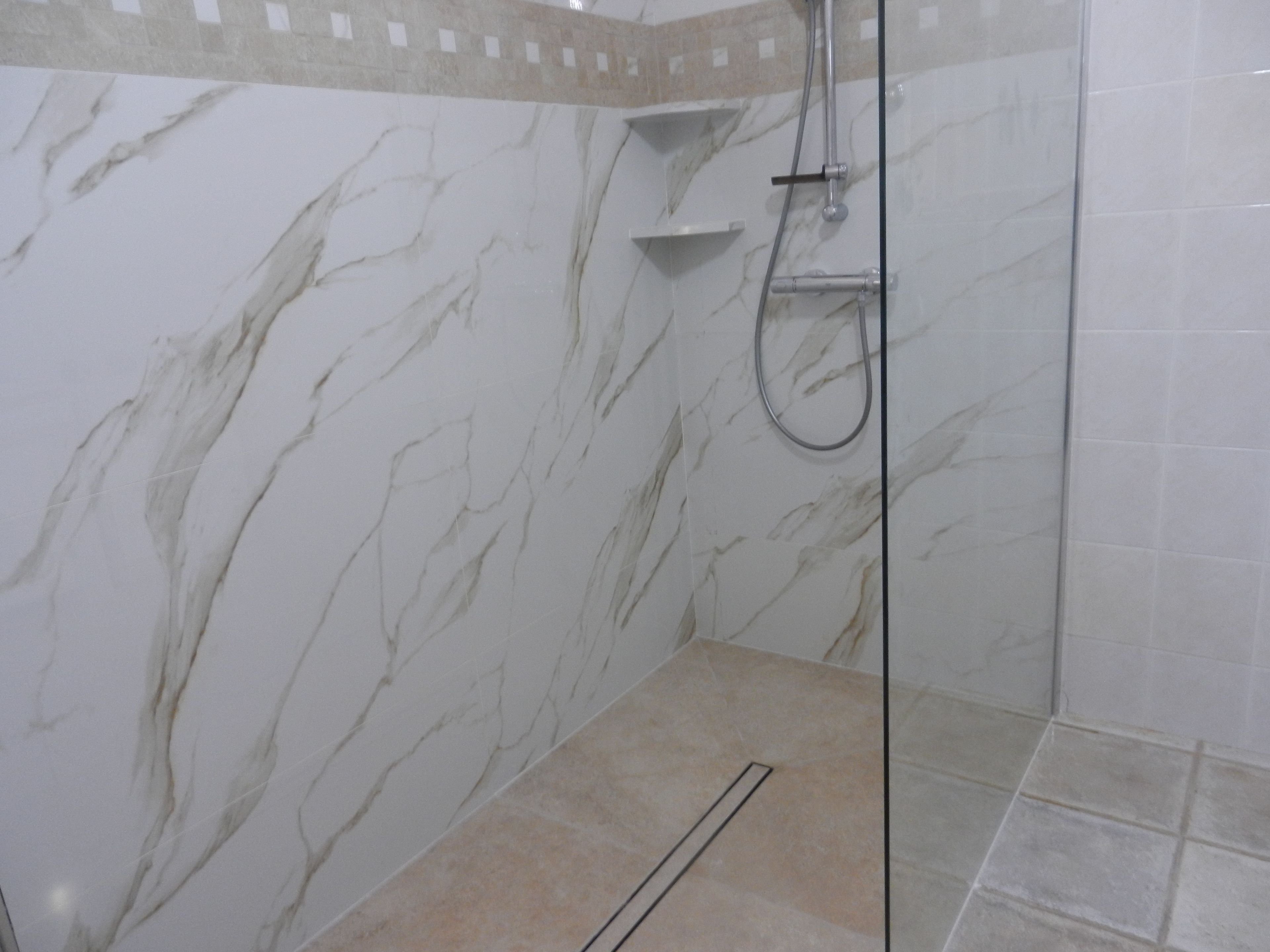 Une salle de bain avec des murs en marbre, un espace douche et un sol carrelé.