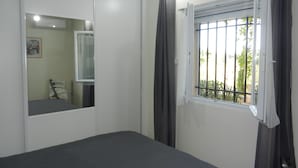 Un dormitorio con cama, ventana con vistas a vegetación, espejo y puerta.