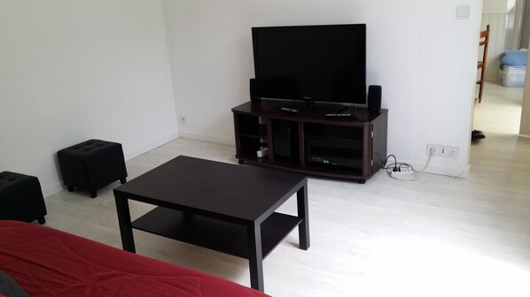 Un salon avec un téléviseur à écran plat posé sur un meuble en bois, une table basse noire et un canapé rouge.