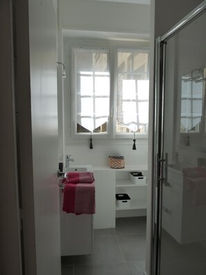 A modern bathroom with white fixtures, a glass shower enclosure, and a window with a view of the outside.