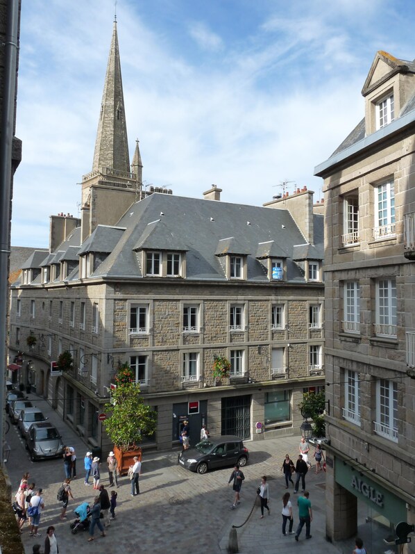 A historic stone building with a prominent tower, a courtyard with pedestrians, and a car parked outside.