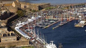 Een jachthaven met veel boten afgemeerd, een groot kasteelachtig gebouw, en een weg naar de jachthaven.