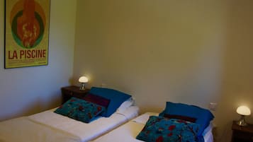 Een hotelkamer met twee bedden, elk met een bloemenkussen en een nachtkastje met een lamp. Een poster aan de muur luidt