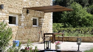 En bygning i sten med pergola, udendørs siddepladser og udsigt over en vingård.