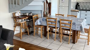 A dining area with a table set for four, a wooden chair, a small table with a glass top, and a staircase leading to another room.