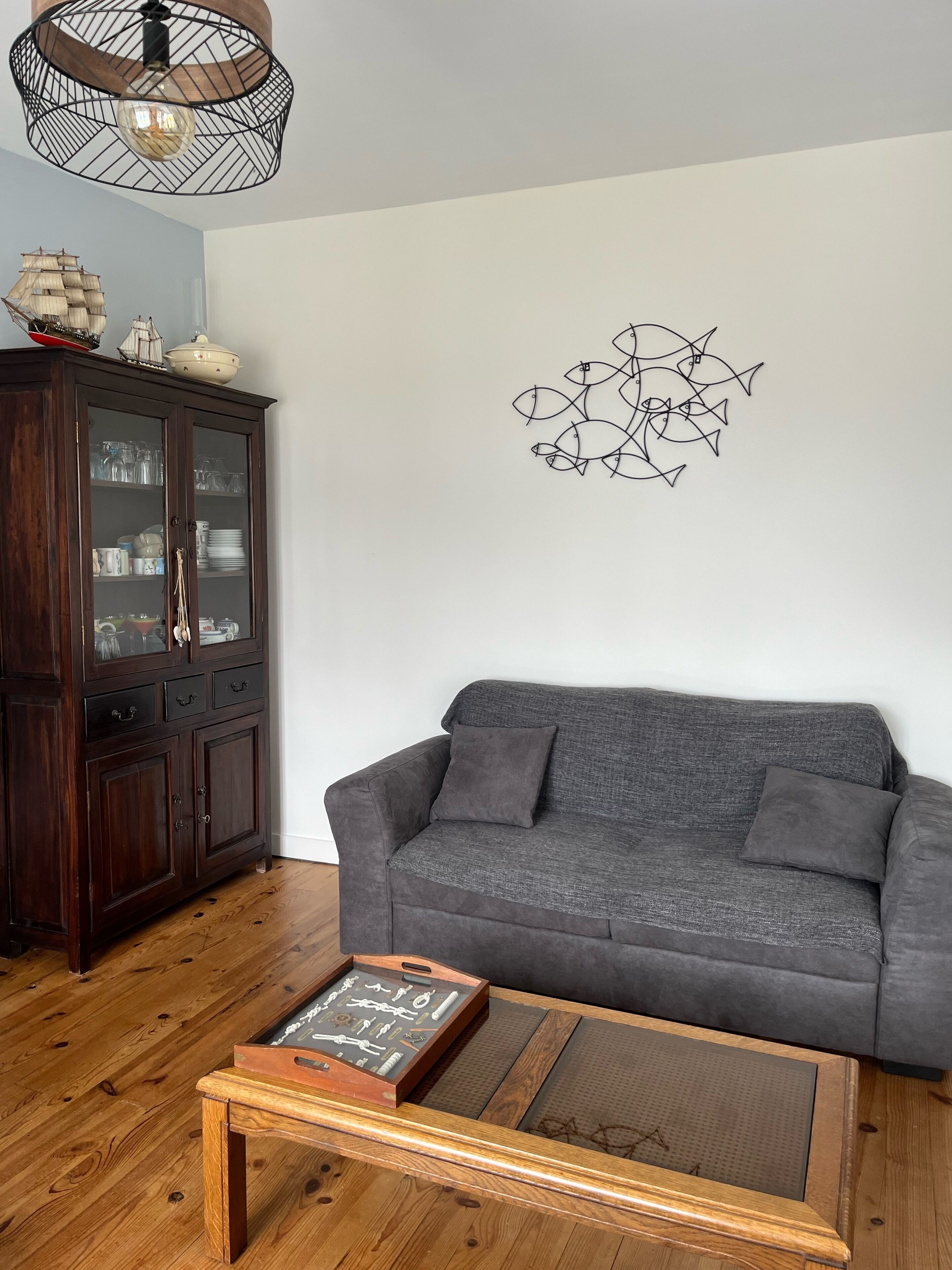 A living room with a dark wooden cabinet, a grey sofa, a wooden coffee table, and a wall art piece.