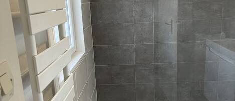 A modern bathroom with a shower area, dark tiled walls, and a wooden floor.