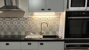 A modern kitchen with grey cabinets, a stainless steel range hood, a microwave, and a dishwasher.