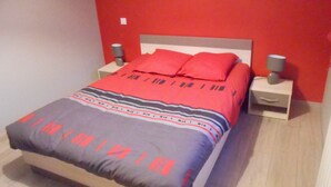 A bed with a red and grey patterned bedspread, two red pillows, and two bedside tables with lamps. - duplex apartment bis (Vannes)