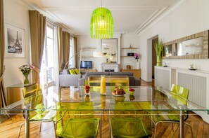 A modern living room with a glass dining table, green chairs, a sofa, a TV, and a bright green pendant light. - LUXURY SECURED SAINT GERMAIN DES PRES (968 Sqf) (Paris)