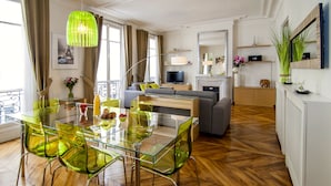 A modern living room with a glass dining table, green chairs, a sofa, and a TV. - LUXURY SECURED SAINT GERMAIN DES PRES (968 Sqf) (Paris)