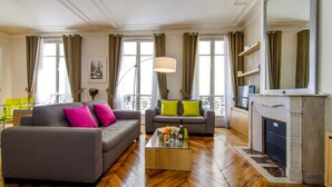 A spacious living room with two sofas, a coffee table, a fireplace, and large windows with curtains. - LUXURY SECURED SAINT GERMAIN DES PRES (968 Sqf) (Paris)