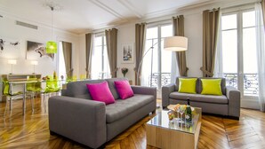 A modern living room with two sofas, a glass coffee table, and a dining area with a glass table and chairs. - LUXURY SECURED SAINT GERMAIN DES PRES (968 Sqf) (Paris)