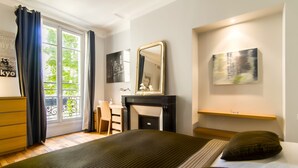 A hotel room with a large bed, a desk, a fireplace, and a view through a window with curtains. - LUXURY SECURED SAINT GERMAIN DES PRES (968 Sqf) (Paris)