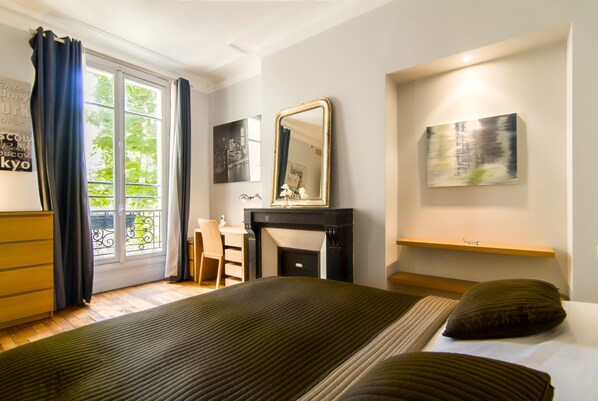 A hotel room with a large bed, a desk, a fireplace, and a view through a window with curtains.