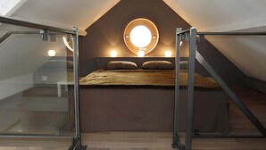Un dormitorio con tragaluz, una ventana circular y una cama con almohadas.