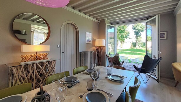 A dining area with a table set for four, a large mirror, and a view of the outdoors. - Villa Le Petit Bois - 2 mns walk Sword beach -Large enclosed garden - Car park (Hermanville-Sur-Mer)