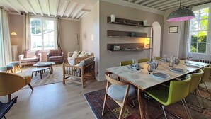 A dining area with a table set for four, surrounded by chairs, and a sofa in the background. - Villa Le Petit Bois - 2 mns walk Sword beach -Large enclosed garden - Car park (Hermanville-Sur-Mer)