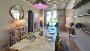 A dining area with a table set for four, a hanging pendant light, a mirror, and a view of the outdoors through a window. - Villa Le Petit Bois - 2 mns walk Sword beach -Large enclosed garden - Car park (Hermanville-Sur-Mer)