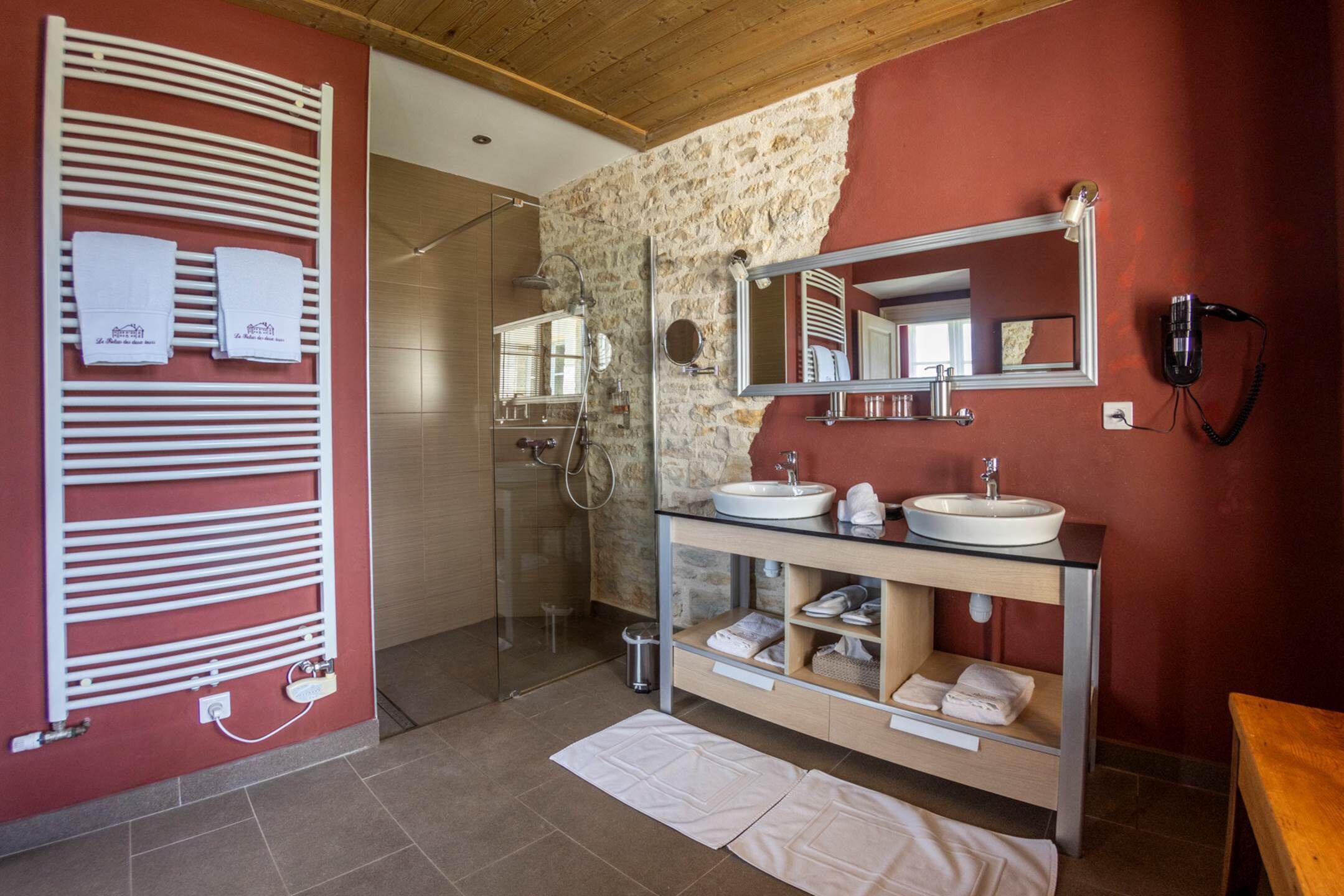 Baño con pared de piedra, cabina de ducha de vidrio, tocador con espejo y perchero para toallas.