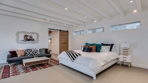 A modern bedroom with a large bed, a sofa, and a coffee table. There is a wooden door and a window with a view. -  5 bdrm, 3.5 bth Private Luxury retreat with mountain views! Permit #068365 (La Quinta)