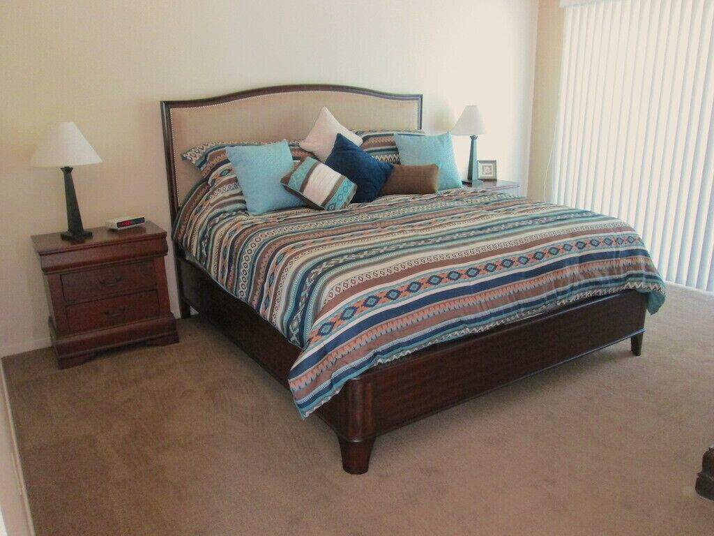 A bedroom with a wooden bed, patterned bedspread, two bedside tables with lamps, and a nightstand with a clock.