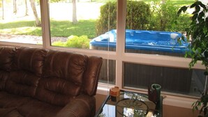 Ein Wohnzimmer mit braunem Ledersofa, einem Glastisch und Blick auf einen Hinterhof mit Whirlpool.