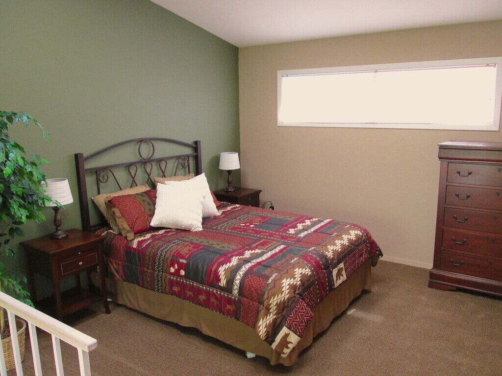 A bedroom with a bed, nightstands, a dresser, a window, and a plant.