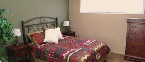 A bedroom with a bed, nightstands, a dresser, a window, and a plant.