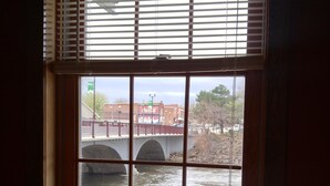 Una ventana con vista a un puente sobre un río, con edificios y árboles al fondo.